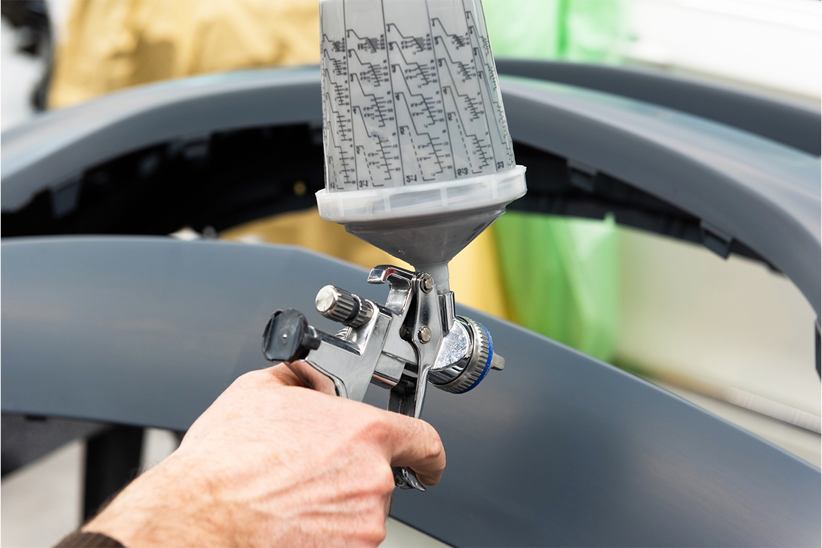 Lackierpistole mit Autoteil im Hintergrund